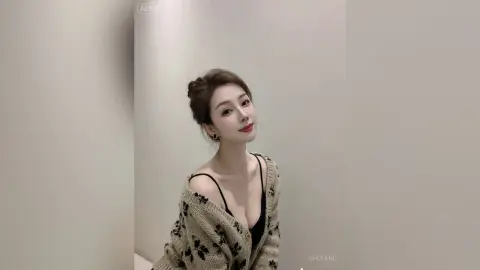 Smiling young woman in a cozy floral cardigan and black camisole posing in a bright minimalist room.