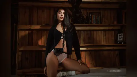 Moody portrait of a brunette woman in black cardigan and white lingerie sitting in a rustic wooden room.