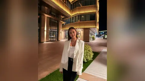 KaranAreas poses in a white blazer and black pants outside a modern building at night.
