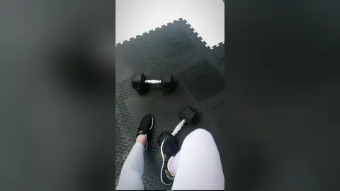 Person in white leggings holding a black dumbbell during a home gym workout session.