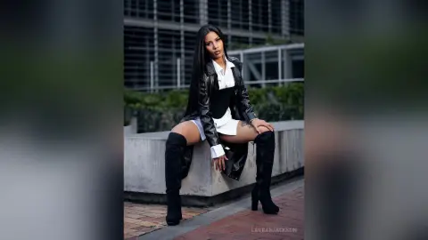 Stylish woman in a black leather jacket and white shirt sitting on a concrete ledge in an urban setting.