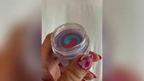 MnemoZeina holds a clear jar containing a swirl of pink and blue liquid or gel against a plain white background.