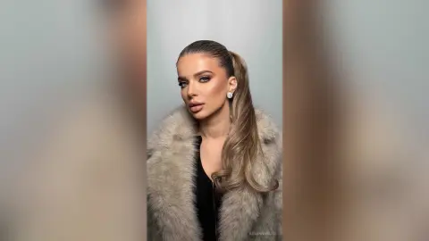 Elegant woman in a luxurious faux fur coat posing with a sophisticated look against a neutral background.