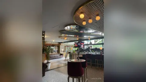 LaraOlson in a modern, upscale lounge or bar setting with warm hanging lights, a dark red velvet chair, and a black and white tiled floor.