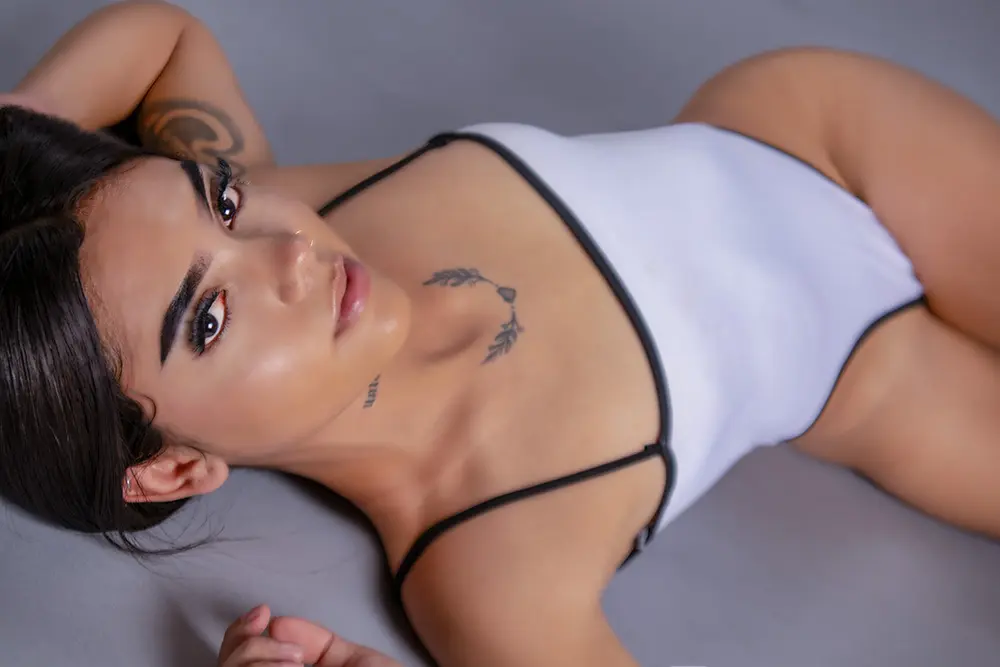 Candymorggan lies on her back wearing a white bodysuit with black trim, looking up at the camera.