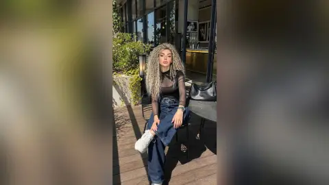 Stylish woman in a black mesh top and blue jeans sitting at an outdoor cafe terrace on a sunny day.