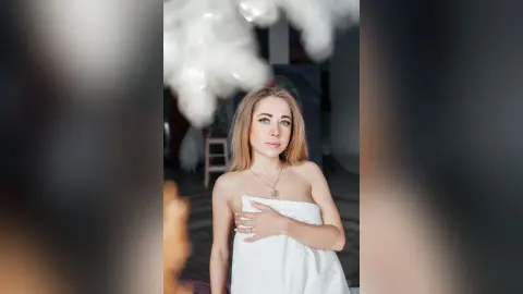 Blonde woman in a white towel relaxing in a bright, dreamy spa setting with a serene mood.