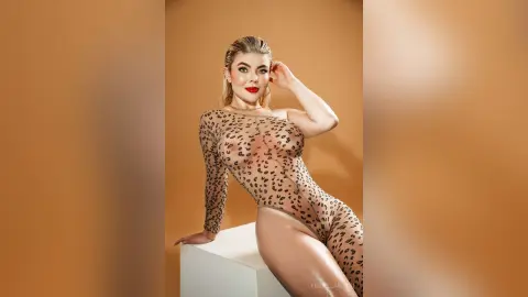 FiorellaRossi poses in a long-sleeve leopard print sheer bodysuit against a tan background.