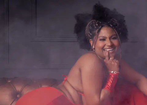 Smiling woman in a red outfit sitting on a vintage sofa in a dreamy, misty studio setting.