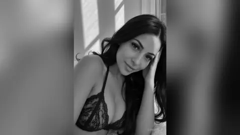 Moody black and white portrait of a woman with long dark hair wearing black lace lingerie in soft sunlight.