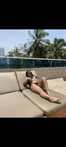 Relaxed woman in a black bikini lounging on a sunbed at a tropical outdoor poolside resort.