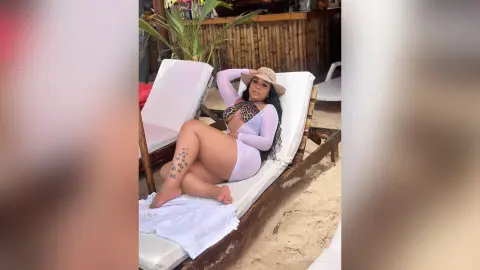 Curvy woman in a white swimsuit and sun hat relaxing on a beach lounge chair under sunny tropical vibes.