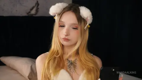 Blonde woman in white bunny ears and lace outfit posing in a cozy bedroom setting.