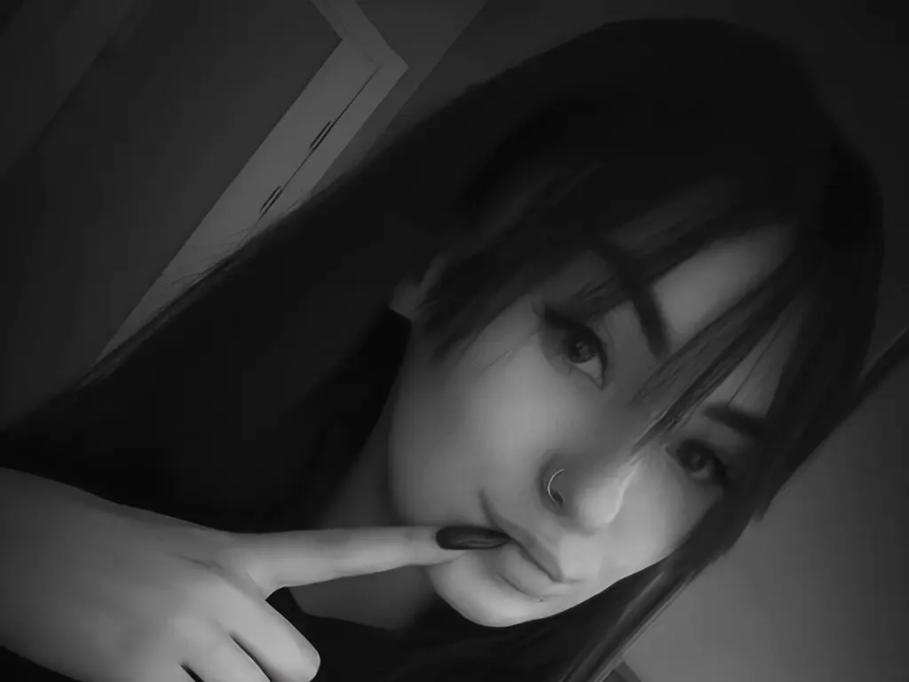 Close-up moody black and white portrait of a young woman with long dark hair and a nose ring.