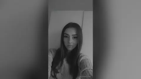 Young woman with long dark hair wearing a cozy ribbed sweater in a minimalist indoor setting with a moody vibe.