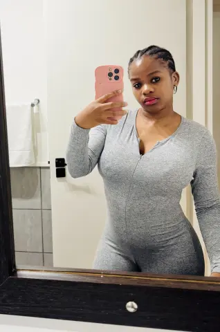 Young woman in a grey long-sleeve bodysuit taking a confident mirror selfie in a modern bathroom.