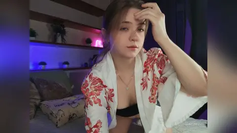 Young woman in a white floral kimono robe relaxing in a bedroom with moody purple ambient lighting.