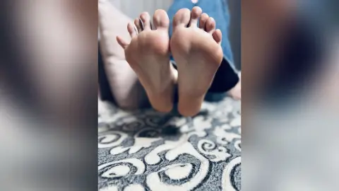 Close-up of bare feet resting on a patterned grey rug in a cozy, relaxed indoor setting.
