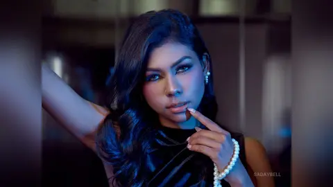 Elegant woman in a black velvet top with pearl jewelry posing in moody, cinematic blue lighting.