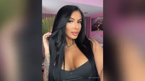 Glamorous woman with long black hair in a black top posing in a pink aesthetic bedroom.
