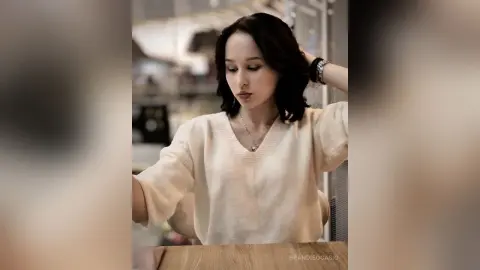 Elegant woman in a white v-neck sweater relaxing in a bright, modern cafe setting.