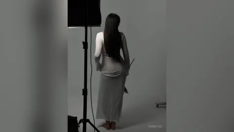 EmmyLee — EmmyLee stands with her back to the camera in a tight, long-sleeved white dress against a grey studio background.