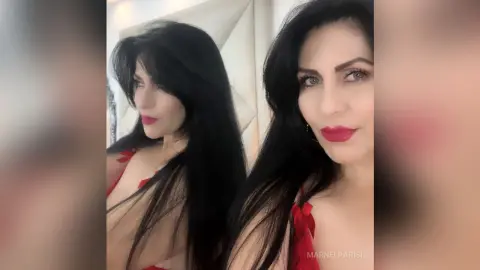 Glamorous woman with long black hair and red lipstick wearing a red outfit in a bright indoor setting.