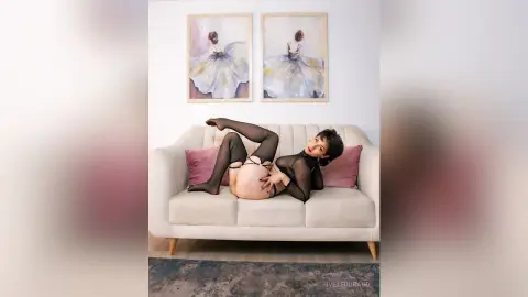 IveteDurand lies back on a white sofa, wearing black sheer lingerie and stockings while exposing her bare buttocks and pussy.