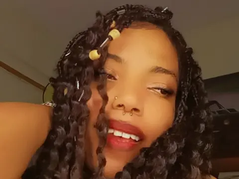 Young woman with long dark braids and nose ring smiling in a warm indoor setting.