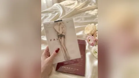 AlienaMoore — AlienaMoore holds a Falke fashion magazine over white satin sheets next to pink roses.