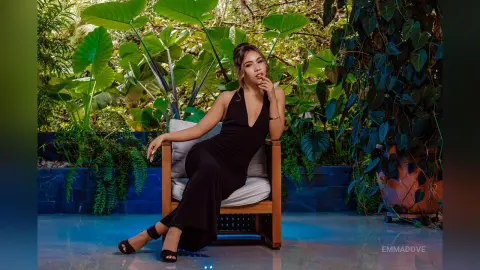 Elegant woman in a black evening dress sitting in a lush tropical garden setting with a serene mood.