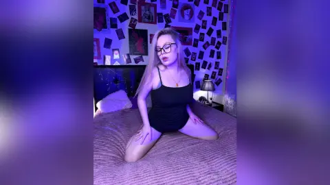 Young woman in a black bodysuit sitting on a bed in a room with purple mood lighting and wall posters.