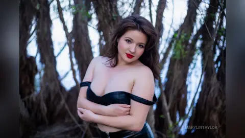 Beautiful woman in a black strapless top posing in a dreamy, sunlit forest setting.