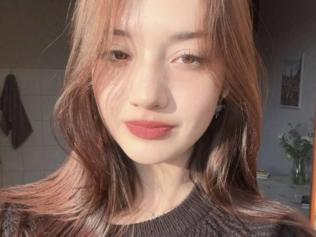 Close-up portrait of a young woman with long wavy hair and red lipstick in soft natural lighting.