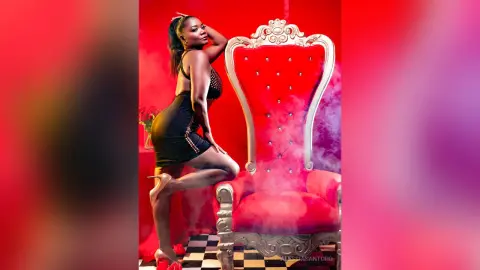AlessiaSantoro — Elegant Black woman in a black cocktail dress posing confidently on a red velvet throne amidst mystical smoke.