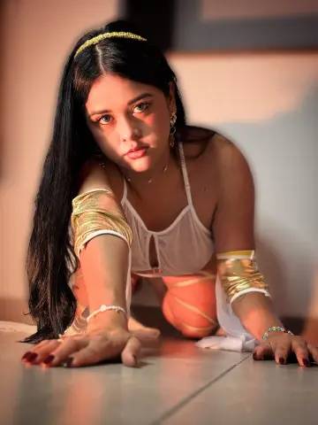Young woman in white and gold bohemian outfit posing on a floor with warm sunset lighting.