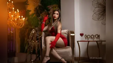 Elegant woman in a red evening dress and gloves sitting in a luxury lounge with a glass of wine.