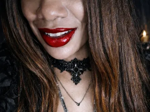 Smiling woman with red lipstick wearing a black lace choker and silver necklace in a moody setting.
