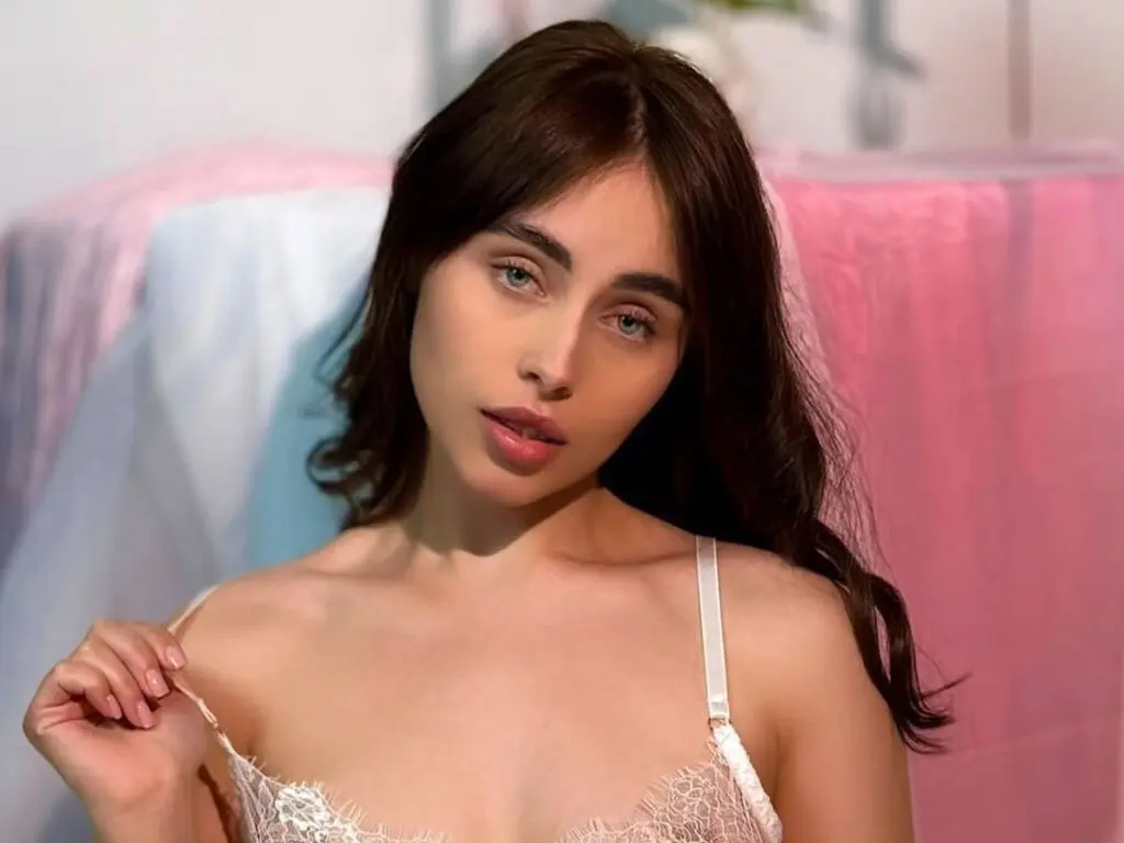 Young woman in white lace lingerie posing in a soft, dreamy setting with pink fabric decor.