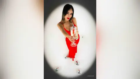 Elegant woman in a red evening dress holding a champagne glass in a glamorous, celebratory setting.