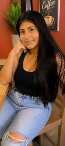 Kendra_Foox poses with long black hair, wearing a black tank top and ripped blue jeans while sitting at a wooden table.