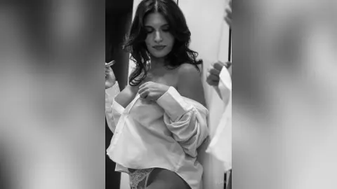 Moody black and white portrait of a woman in an oversized white button-down shirt in a soft indoor setting.