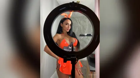 Beautiful woman in an orange bunny costume posing for a selfie in a modern bathroom using a ring light.