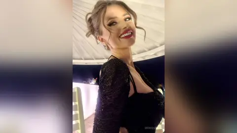 Smiling young woman in a sparkling black sequin evening dress posing in a dimly lit venue.