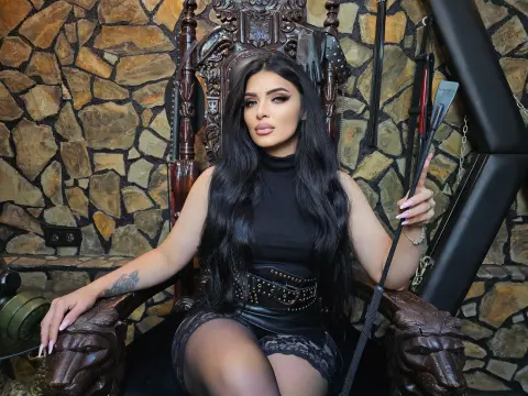 Elegant woman in a black turtleneck and leather skirt sitting on a gothic throne against a stone wall.