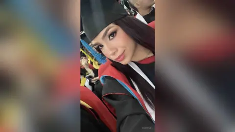 KimRece smiles wearing a black graduation cap and gown with red and blue trim.