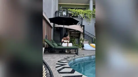 KeianHoz sits on a green lounge chair by a swimming pool, wearing a white bikini and facing away from the camera.