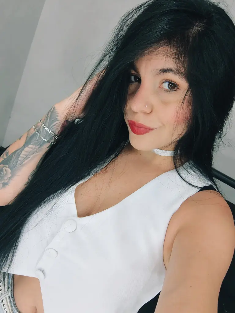 LustyQueen_777 poses with long black hair, wearing a black sleeveless bodysuit and sheer black tights against a white background.