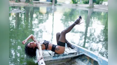 Woman in black lingerie relaxing on a small boat in a serene, misty lake setting.