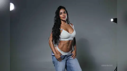 Confident woman in white Calvin Klein underwear and blue jeans posing in a studio setting.